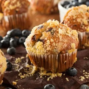 Golden blueberry flax muffins topped with streusel, surrounded by fresh blueberries.