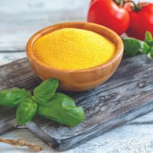 Wooden bowl of organic yellow cornmeal with basil and tomatoes on rustic board