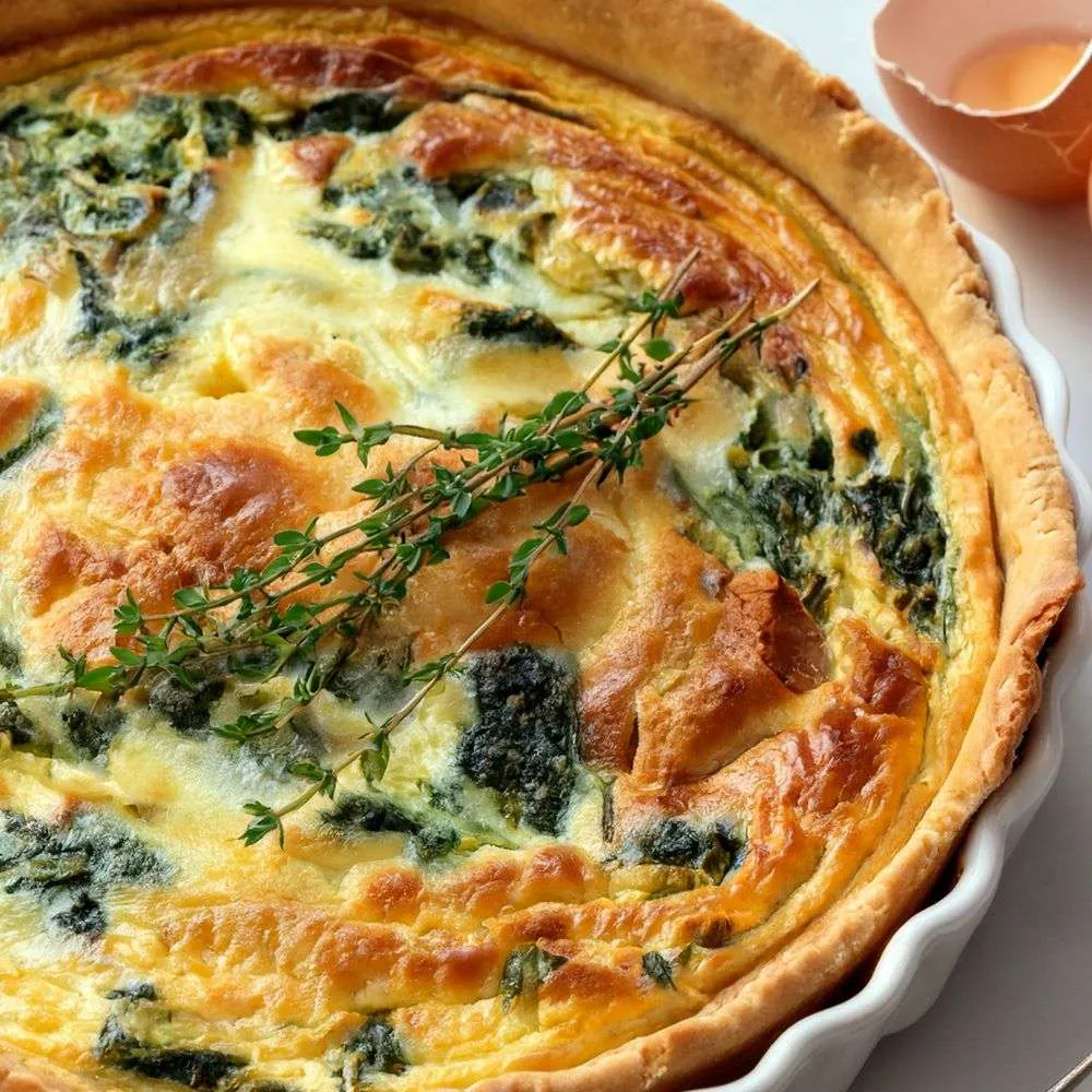 Golden baked spinach and cheese quiche in a flaky organic crust, garnished with fresh thyme.