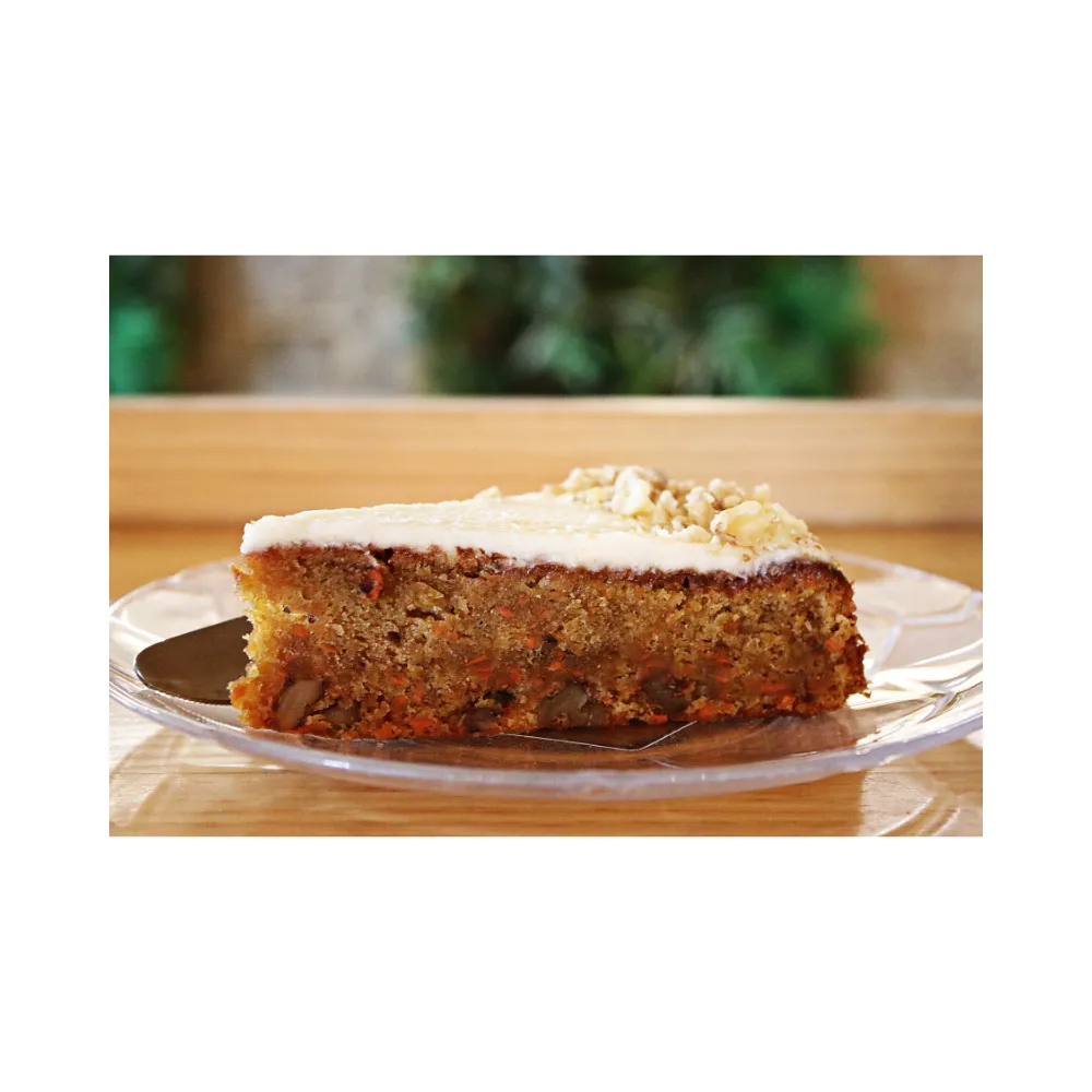 Slice of homemade carrot cake with cream cheese frosting, served on a clear glass plate.